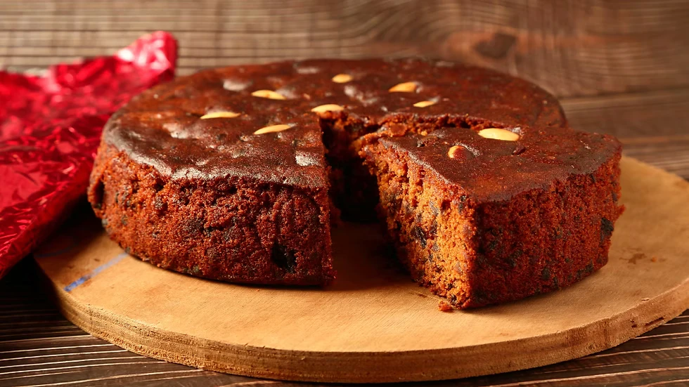 A whole plum cake with one slice cut, on a wooden board